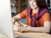 student in orange shirt looking at laptop screen